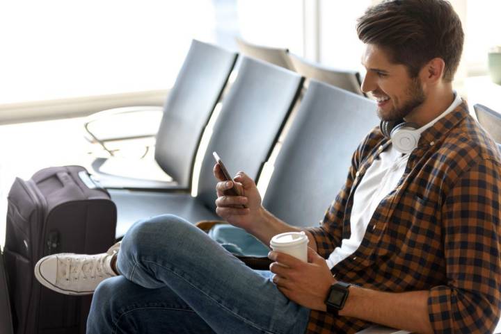 Un chico joven esperando el avión junto a su maleta.