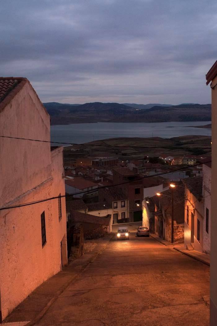 Calles desiertas al caer la noche en Peñalsordo, con el pantano al fondo.